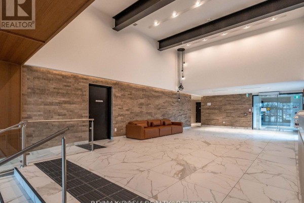 Spacious lobby with white marble floors, a brick accent wall, and a brown leather sofa. - 723 - 2300 St Clair Avenue W, Toronto