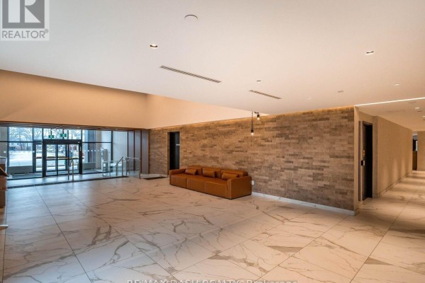 Wide view of a modern lobby with marble tile floors, brick walls, and multiple doorways. - 723 - 2300 St Clair Avenue W, Toronto