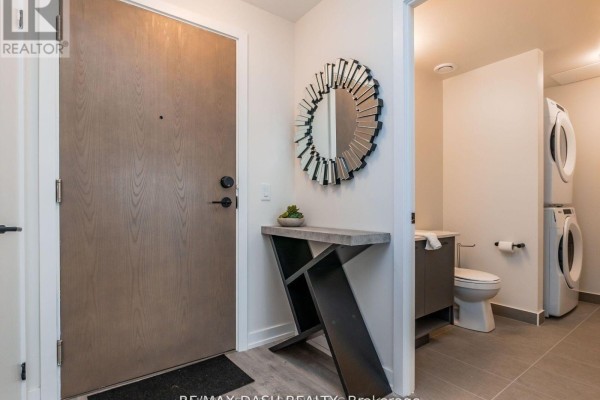 Entrance area with a wooden door, console table, mirror, toilet, and stacked washer and dryer. - 723 - 2300 St. Clair Avenue W, Toronto