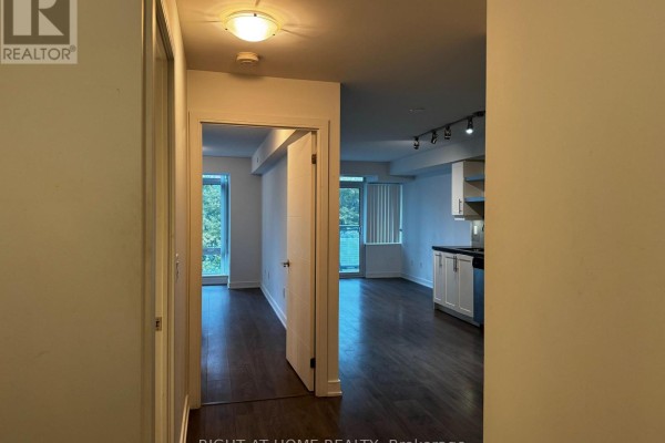 View from hallway towards an open-concept living area and kitchen with dark wood flooring and large windows. - 723 - 525 Adelaide Street W, Toronto