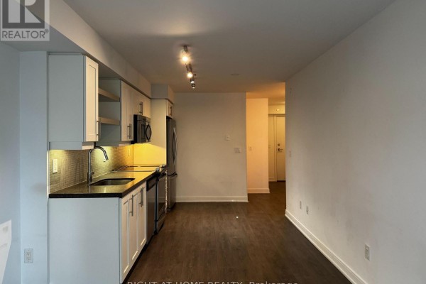View of the kitchen and living area from the side, showing dark wood flooring and white walls. - 723 - 525 Adelaide Street W, Toronto