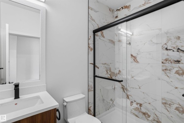 A compact bathroom with a white toilet, vanity, and a large marble-tiled shower stall. - 723 158 Av Ne, Edmonton