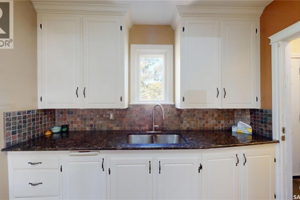 Close-up of the kitchen sink area with granite countertops and a mosaic tile backsplash. - 723 9th Street E, Saskatoon