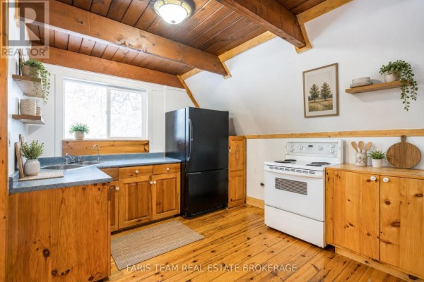 Kitchen with wood cabinets, a black refrigerator, white stove, and wood plank floors. - 7237 6/7 Sideroad Nottawasaga, Clearview