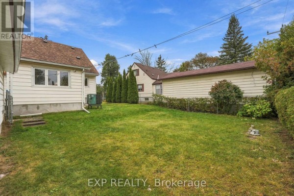 Backyard with green grass, a white siding house, a garage, and tall evergreen trees. - 724 Mckellar Street, Peterborough