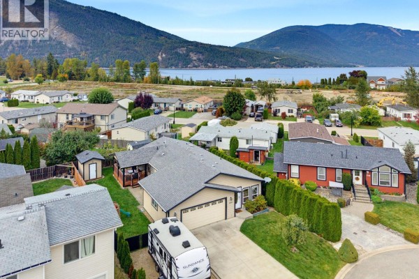 Aerial view of a residential street with a beige single-story house, other homes, and mountains. - 7241 46 Street Ne, Salmon Arm