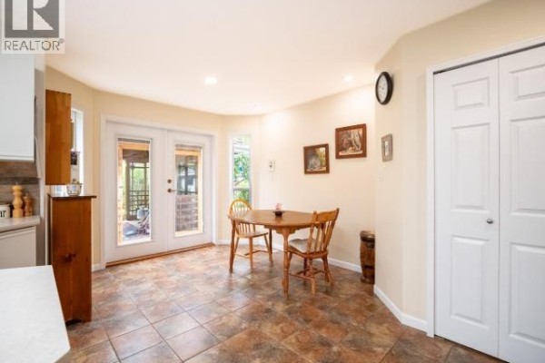 Kitchen nook with a small wooden table, chairs, double glass doors, and closet doors. - 7249 Field Street, Powell River
