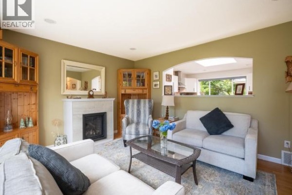 Living room with a fireplace, two sofas, coffee table, armchair, and arched pass-through. - 7249 Field Street, Powell River