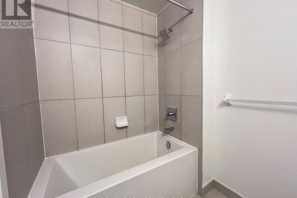 Compact bathroom with a white bathtub, grey tiled walls, and a silver shower fixture and faucet. - 725 - 60 Princess Street, Toronto