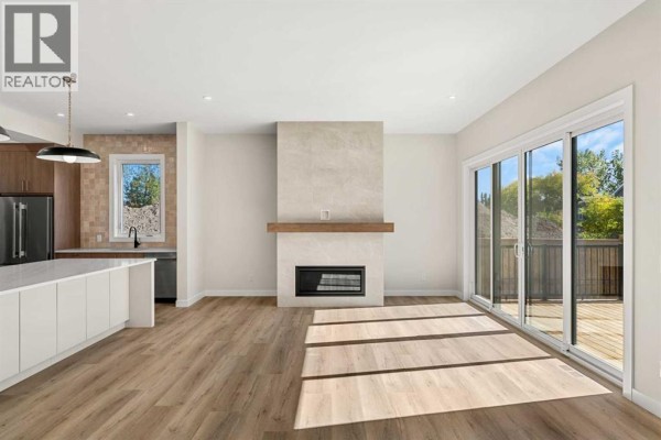 Living room facing kitchen and fireplace with blonde wood floors and large sliding glass doors. - 725 53 Avenue Sw, Calgary