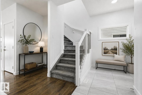 Foyer with dark wood floors and a large round mirror. Staircase with grey carpet and silver railings. - 7258 Chivers Pl Sw, Edmonton