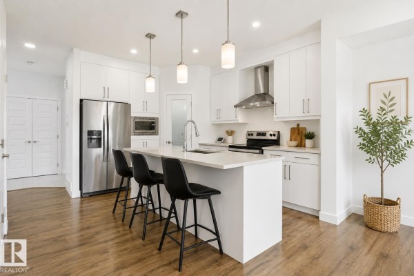 Modern kitchen with white cabinets, quartz countertops, stainless steel appliances, and an island with bar stools. - 7258 Chivers Pl Sw, Edmonton