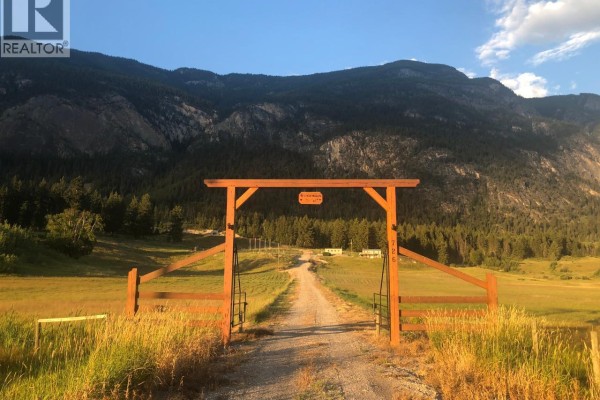Entrance gate leading to gravel driveway with mountains in the background. - 726 95 Highway, Spillimacheen