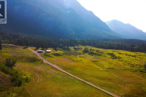 Aerial view of open fields and structures with mountains surrounding the area. - 726 95 Highway, Spillimacheen