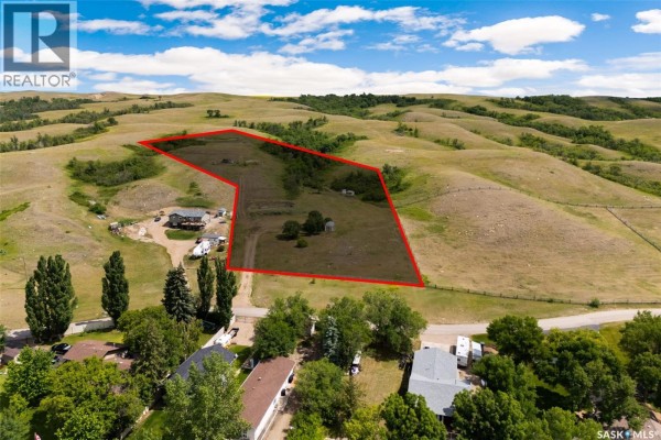 Panoramic view of a wide lake bordered by green trees and homes, with rolling hills in the distance. - 726 Daniel Drive, Buffalo Pound Lake
