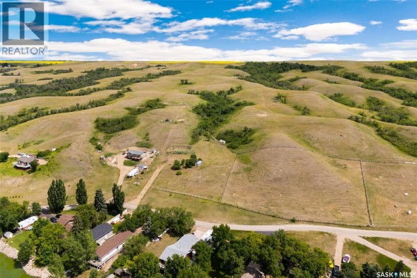 A grassy field with a greenhouse and distant lake view under a partly cloudy sky. - 726 Daniel Drive, Buffalo Pound Lake