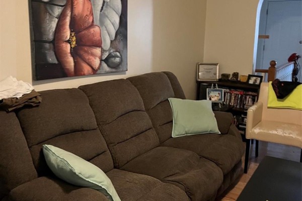 Living room with a brown reclining sofa, light blue pillows, and a beige armchair. - 726 M Avenue S, Saskatoon