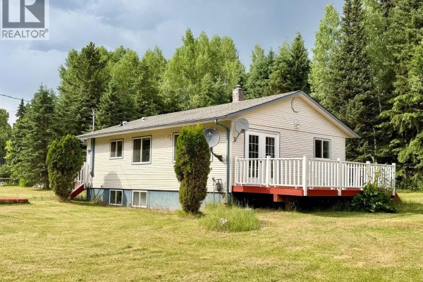 Front exterior of a beige bungalow with red steps leading to the front door and a white deck on the right. - 7280 Otway Road, Prince George