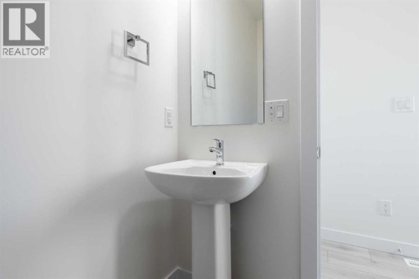Powder room with a pedestal sink and large mirror against a white wall - 729 Clearview Green, Chestermere