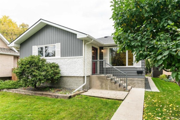Side angle of a grey and white bungalow with a lawn, trees, and a walkway. - 729 Kildonan Drive, Winnipeg