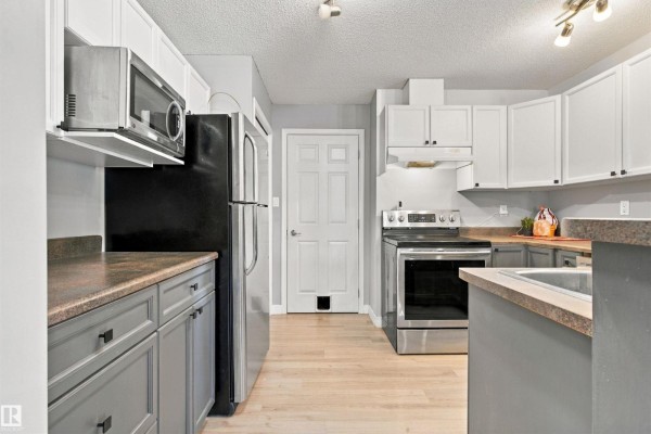 Kitchen with grey and white cabinets, stainless steel refrigerator, microwave, and stove. - #73 3040 Spence Wd Sw, Edmonton