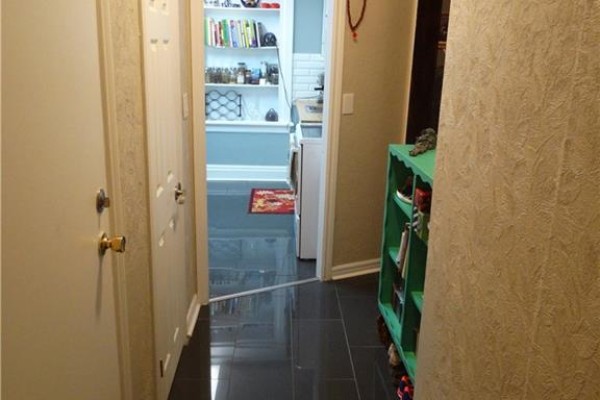 Hallway with dark tile floors, white doors, and a green shelving unit next to patterned wallpaper. - 73 Barnesdale Boulevard Unit# 1, Hamilton