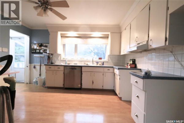 Blue room with light wood laminate flooring, a glass-top desk, and cardboard boxes. - 73 Canwood Crescent, Yorkton