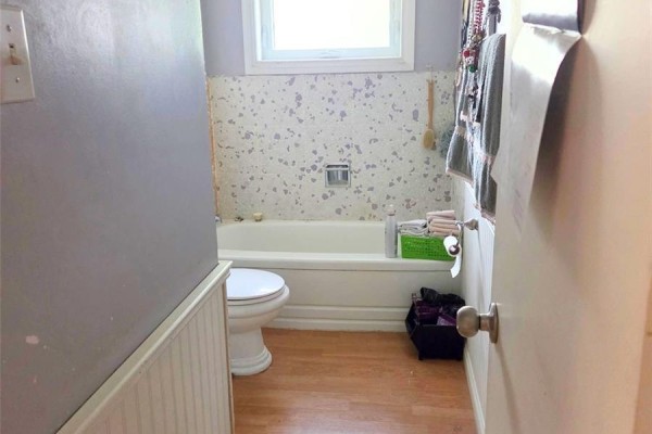 Bathroom with a white bathtub and toilet, light wood laminate flooring, and grey walls. - 73 Canwood Crescent, Yorkton