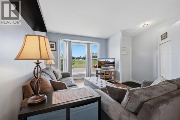Living room with grey sectional sofa, ottoman, and large bay window facing outdoors. - 73 Duncan Crescent, Red Deer