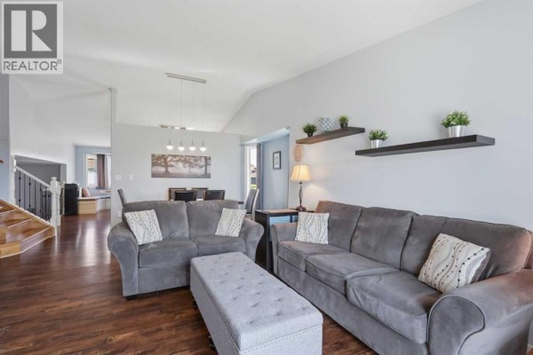 Open concept living and dining area with grey sofas, dark wood floors, and vaulted ceiling. - 73 Duncan Crescent, Red Deer