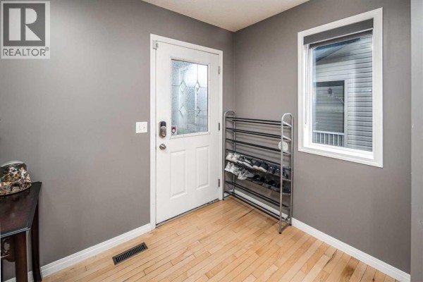 Entryway with grey walls, a white door with frosted glass, and a black shoe rack. - 73 Evansbrooke Way Nw, Calgary