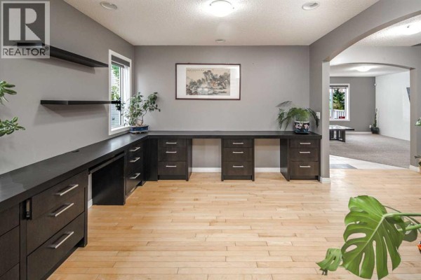 Office space with a long dark wood desk, light wood floors, and grey walls. - 73 Evansbrooke Way Nw, Calgary