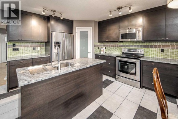 Kitchen with dark wood cabinets, a large island, stainless steel appliances, and a checkered floor. - 73 Evansbrooke Way Nw, Calgary