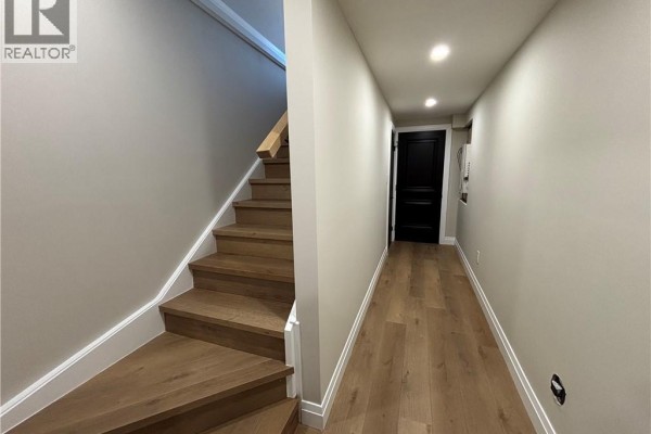 Hallway with light wood flooring, neutral walls, a black door at the end, and recessed ceiling lights. - 73 Mary Street Unit# 1b, Brantford
