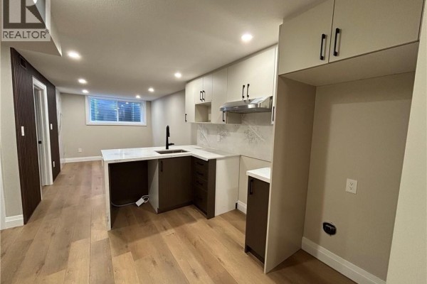 L-shaped kitchen with a white countertop island, dark lower cabinets, and light upper cabinets, adjacent to a living area. - 73 Mary Street Unit# 1b, Brantford