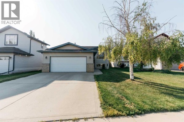 Side view of a beige house showing the double garage, beige siding, and large corner windows. - 73 Ogilvie Close, Red Deer