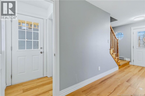 Interior hallway with light wood floors, a staircase, and a white front door with glass panes. - 73 Sawgrass Drive, Riverview
