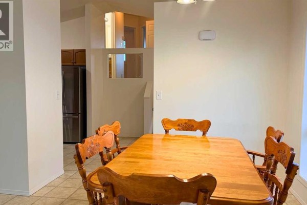 Dining area with a wooden table and chairs, leading to a kitchen with stainless steel appliances. - 7302 104a Street, Grande Prairie
