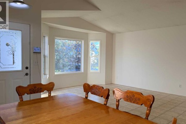Interior view showing a dining table, entryway door, and bay windows with trees outside. - 7302 104a Street, Grande Prairie