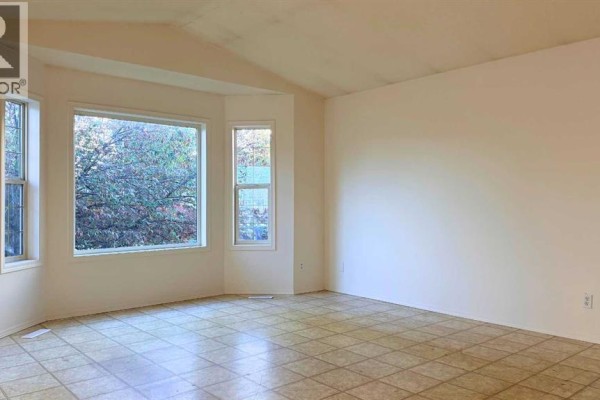 Spacious living area with large bay windows showcasing a view of autumn foliage. - 7302 104a Street, Grande Prairie