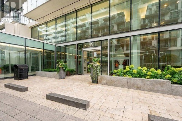 Building entrance with glass doors, signage, planters, and stone patio. - 731 - 39 Queens Quay E, Toronto