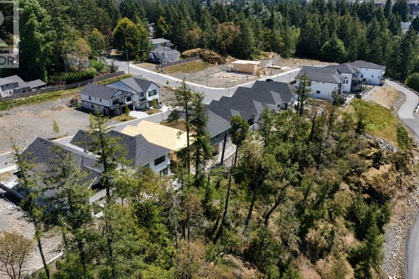Aerial view showing new construction homes nestled amongst tall trees on a sloped residential street. - 731 Madrona Ridge, Langford