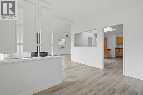 Interior view of a living room with white walls, wood-look flooring, and a partial room divider. - 731 Queensland Drive Se, Calgary