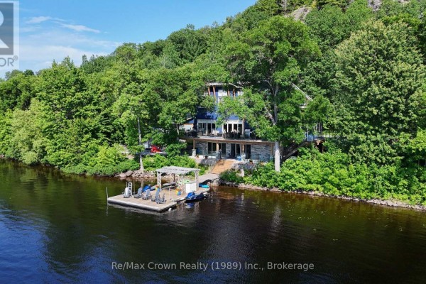 Three-story blue house with stone lower level and glass balconies faces a lake. - 7313 534 Highway, Parry Sound Remote Area