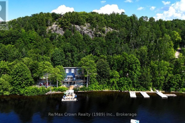 Aerial view of a large blue house on a lake surrounded by trees. - 7313 534 Highway, Parry Sound Remote Area