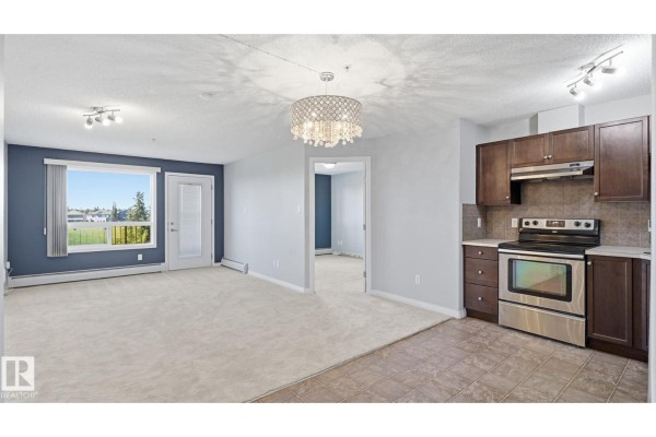 Open concept living room and kitchen with beige carpet and a large window. - #7319 7327 South Terwillegar Dr Nw, Edmonton