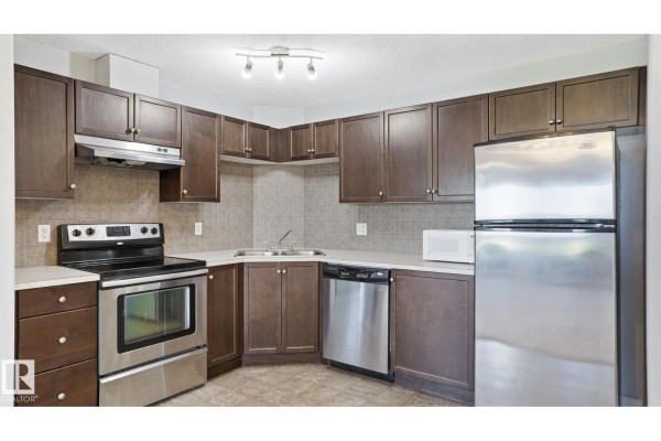 Kitchen with dark wood cabinets, stainless steel appliances, and a beige tiled floor. - #7319 7327 South Terwillegar Dr Nw, Edmonton