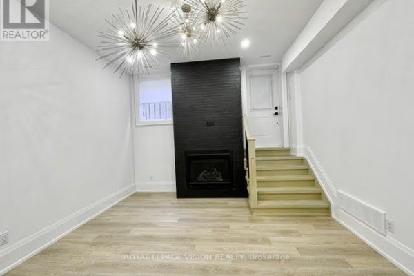 A living area with light wood floors, white walls, and a black fireplace surround, with stairs to the right. - 732 West Shore Boulevard, Pickering