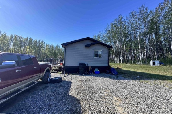 Exterior of a grey modular home with a deck, parked beside a gravel driveway and a red pickup. - 7323 Twp Road 512, Rural Parkland County