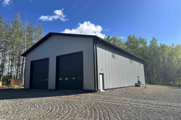Front view of a large, light grey steel building with two dark grey roll-up doors and a small side door. - 7323 Twp Road 512, Rural Parkland County